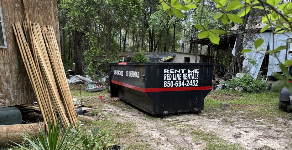 Red Line Rentals roll-off dumpster placed in a wooded backyard for a property cleanout