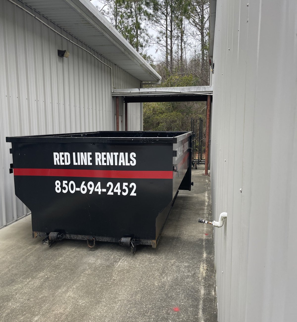 Red Line Rentals roll-off dumpster parked beside a metal building